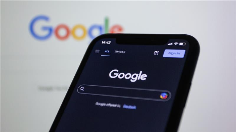 A smartphone displaying the google homepage, with a blurred google search bar as the background - symbolising googles new MUVERA algorithms